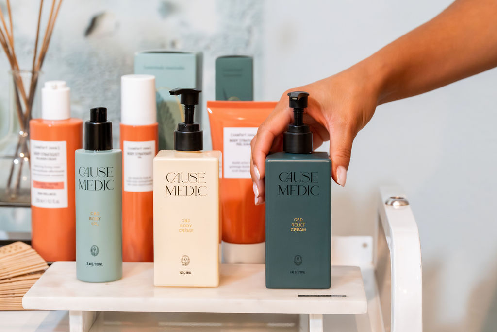 A hand arranges multiple &ldquo;Cause Medic&rdquo; CBD skincare bottles on a shelf in a clean bathroom setting.