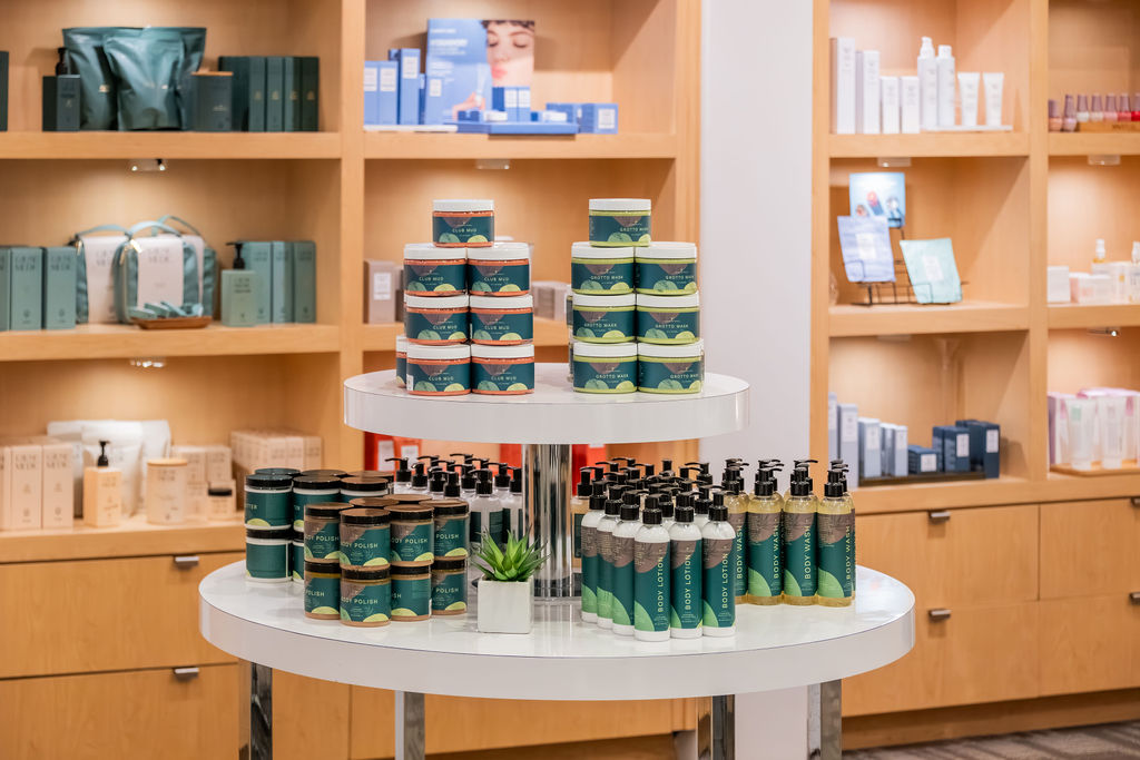 A beauty store shelf display shows stacks of body products and small bottles on a rotating platform in a tidy boutique setting.