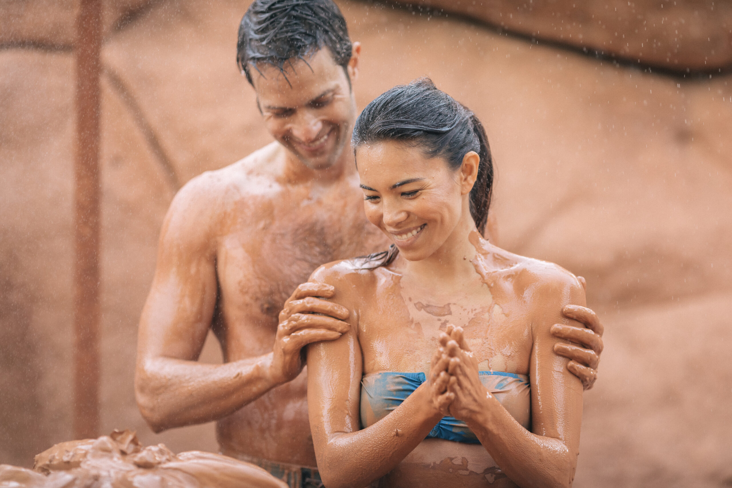 Couple slathering red clay mud on each other while enjoying Glen Ivy Hot Spring's Club Mud.