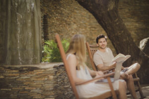 Couple sitting in rocking chairs enjoying their mindful morning together by reading a book and checking emails.